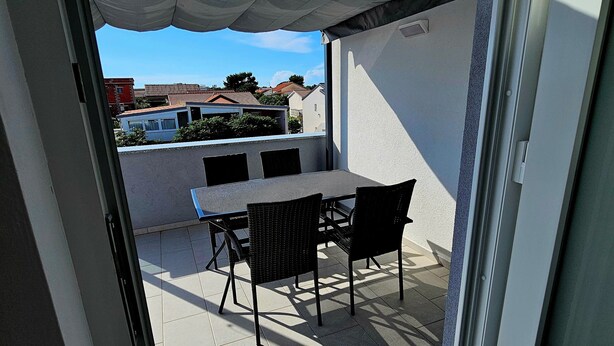 An outdoor patio with a table and chairs, a white canopy, and a view of buildings in the background. - Apartment Jelena, modern new, 200m to the beach, free of charge. W-LAN and parking (Vir)