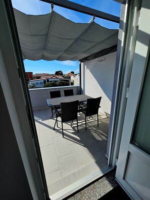 Un patio al aire libre con una mesa y sillas, un toldo blanco y vistas a edificios al fondo.