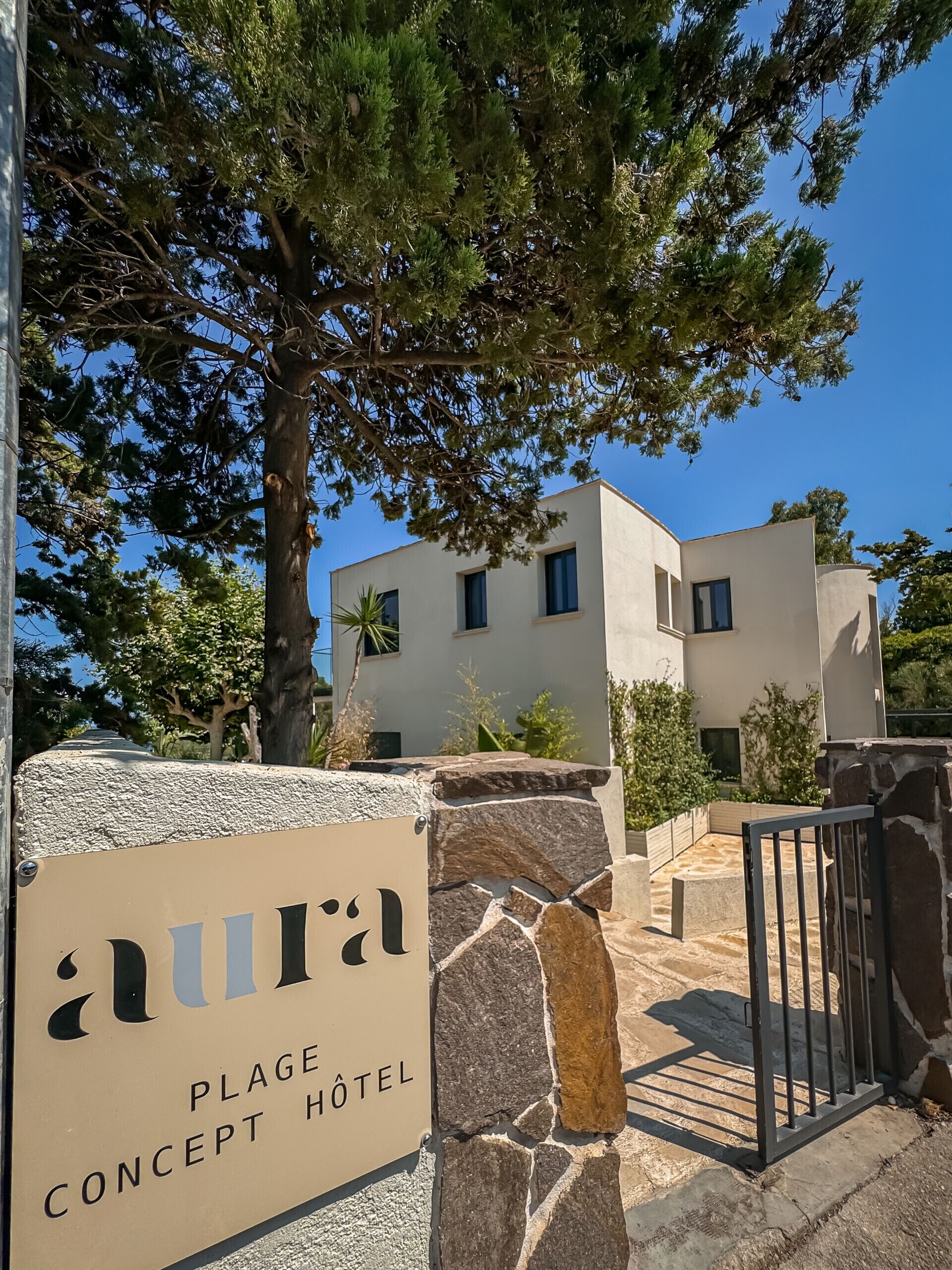 Señal del hotel Plage Concept, con un muro de piedra y una reja de metal.