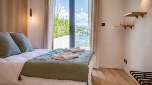 Ein Schlafzimmer mit Bett, Blick auf Grün und Wasser sowie Holzboden.