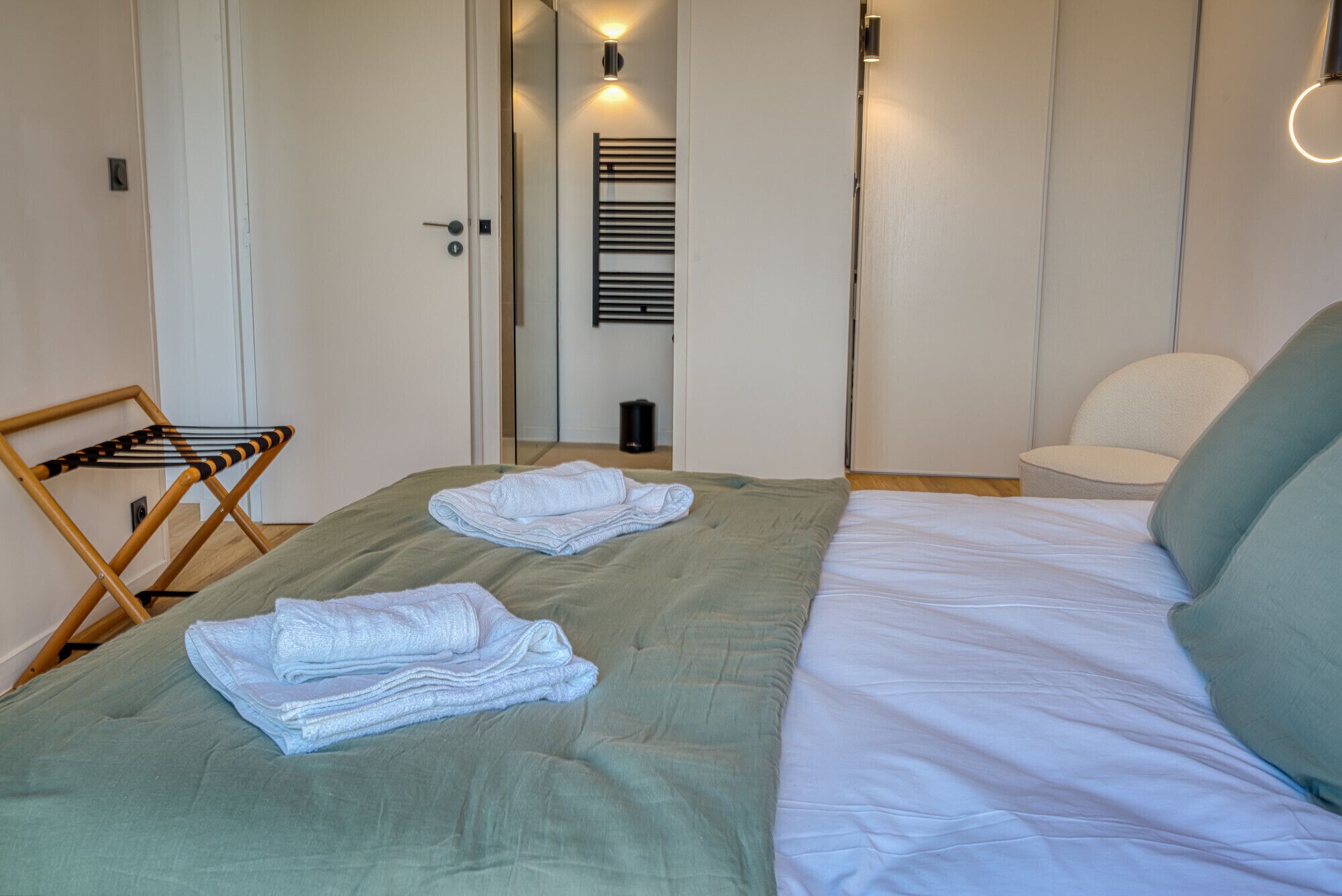 Ein Schlafzimmer mit einem Bett, zwei Handtüchern, einem Stuhl und einer Wandleuchte.