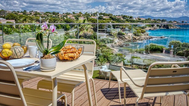 Ein Balkon mit gedecktem Tisch für das Frühstück, mit Blick auf eine Küstenlandschaft mit Häusern und blauem Himmel.