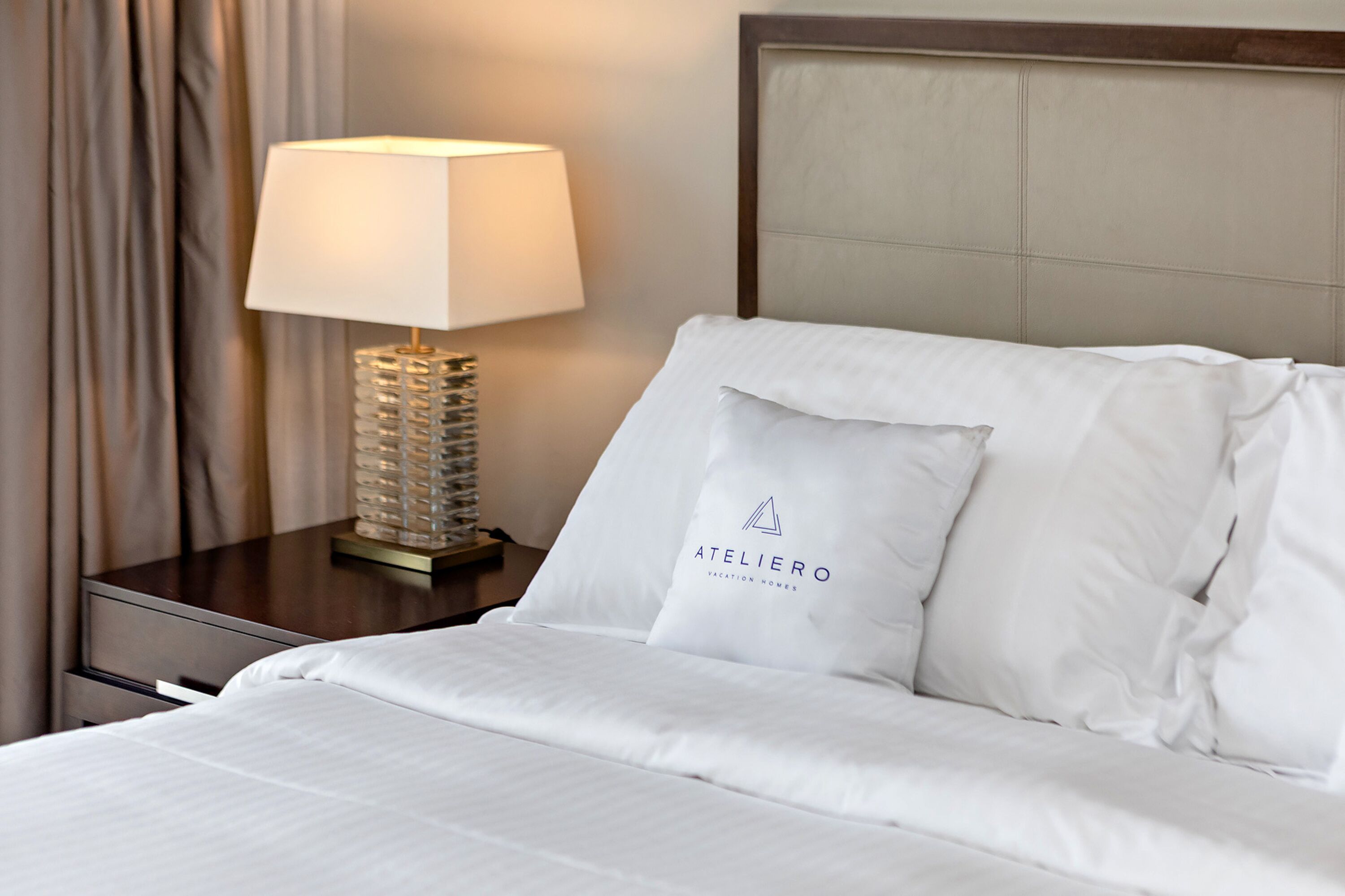 A neatly made bed with white linens and pillows, a bedside lamp, and a nightstand.