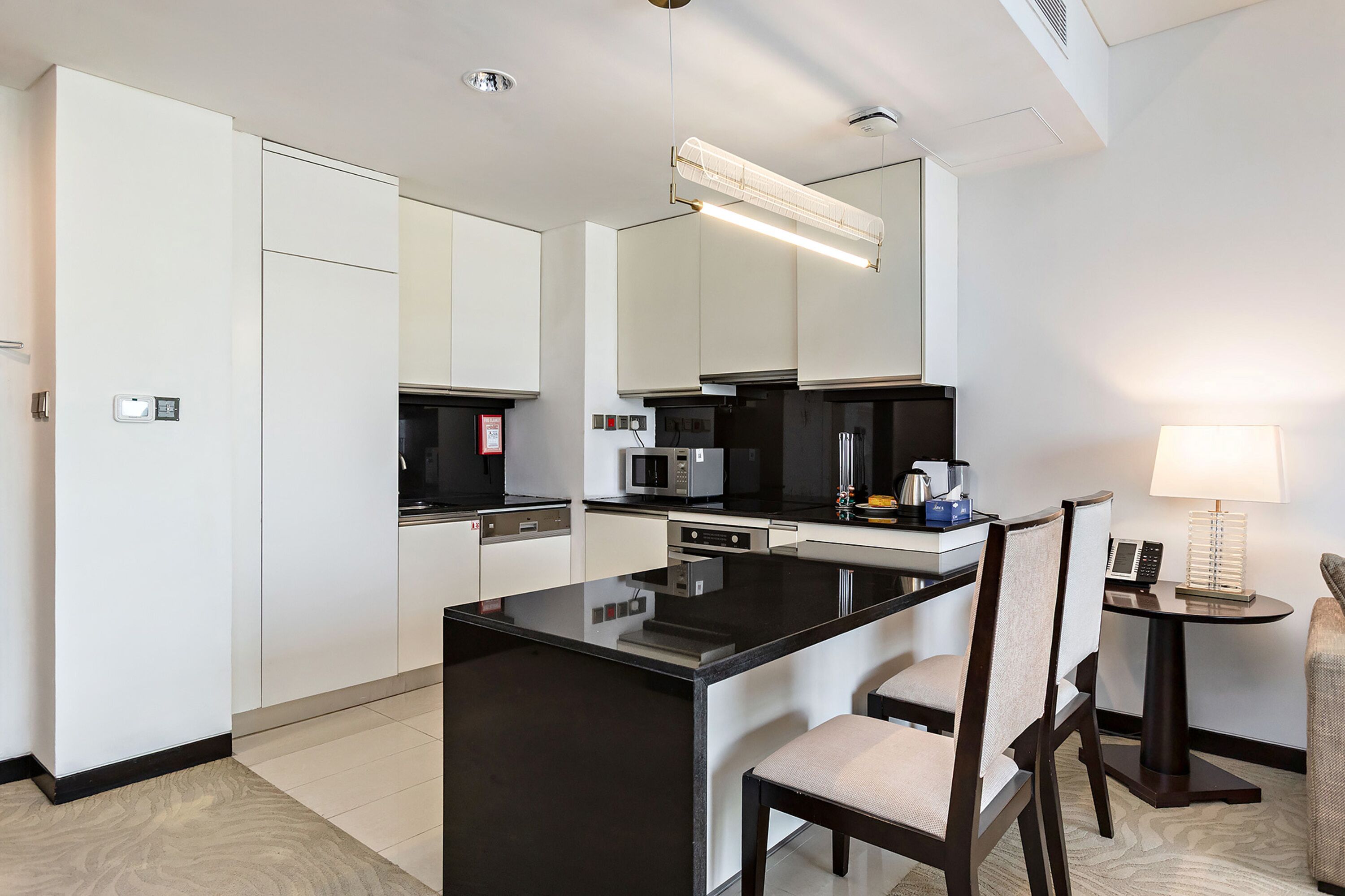 Et moderne hotelkøkken med en central ø, indbyggede hårde hvidevarer og et spiseområde med et bord og stole.