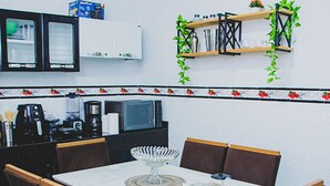 A dining area with a white table, dark chairs, and a kitchen in the background. - Casa Pet Friendly em Condom nio c Vaga em Marituba (Marituba)