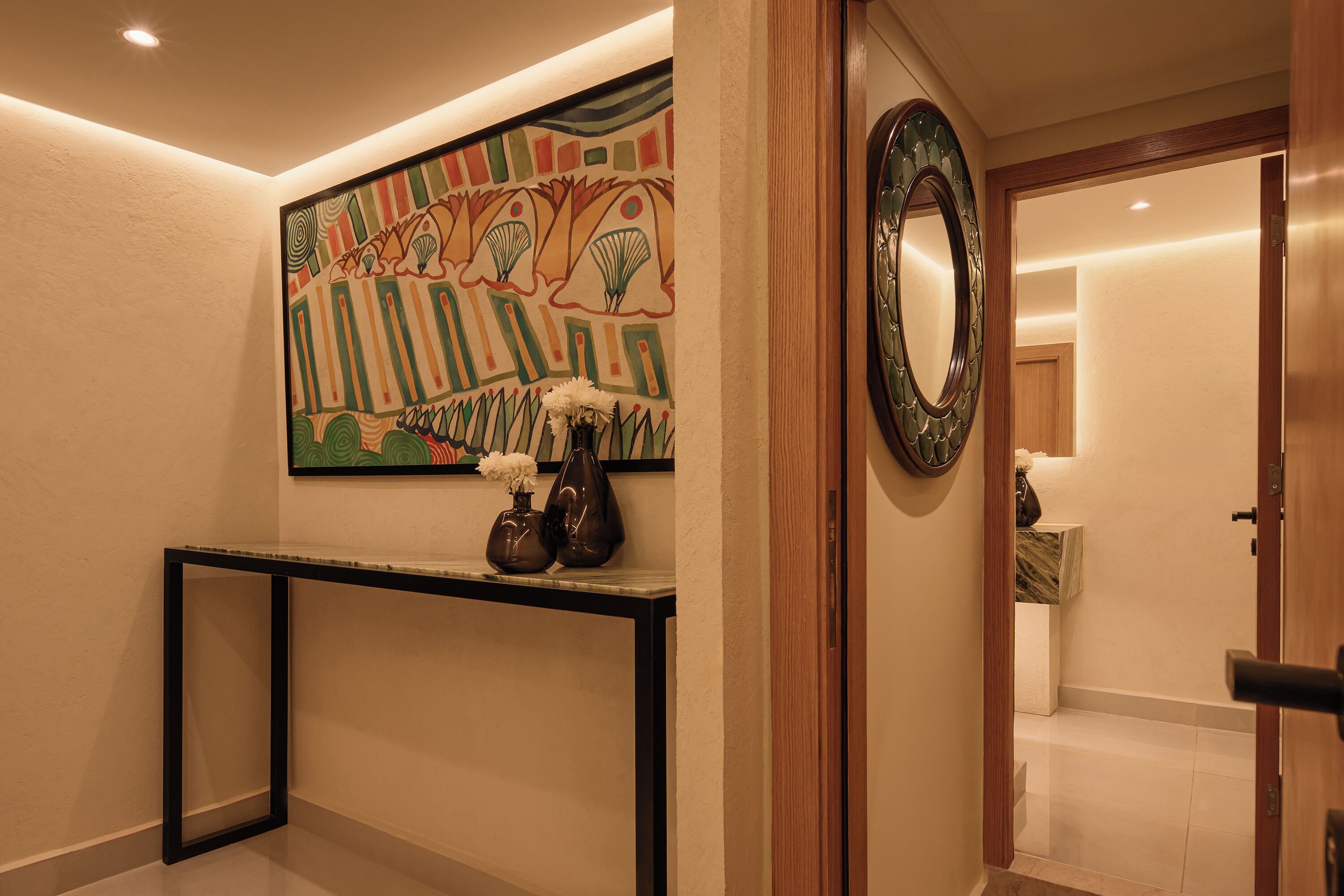 A hallway with a decorative wall, a console table with vases, and a mirror.