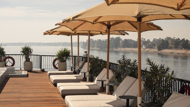 A deck with sun loungers and umbrellas overlooking a body of water. - Le Fayan Suites Nile Cruise - Mondays from Luxor & Fridays from Aswan. (Luxor)