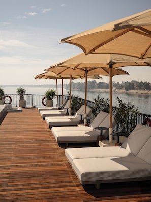 A deck with sun loungers and umbrellas overlooking a body of water. - Le Fayan Suites Nile Cruise - Mondays from Luxor & Fridays from Aswan. (Luxor)