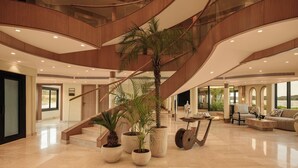 A spacious lobby with a central staircase, multiple potted plants, and a seating area with a view of the outdoors. - Le Fayan Suites Nile Cruise - Mondays from Luxor & Fridays from Aswan. (Luxor)