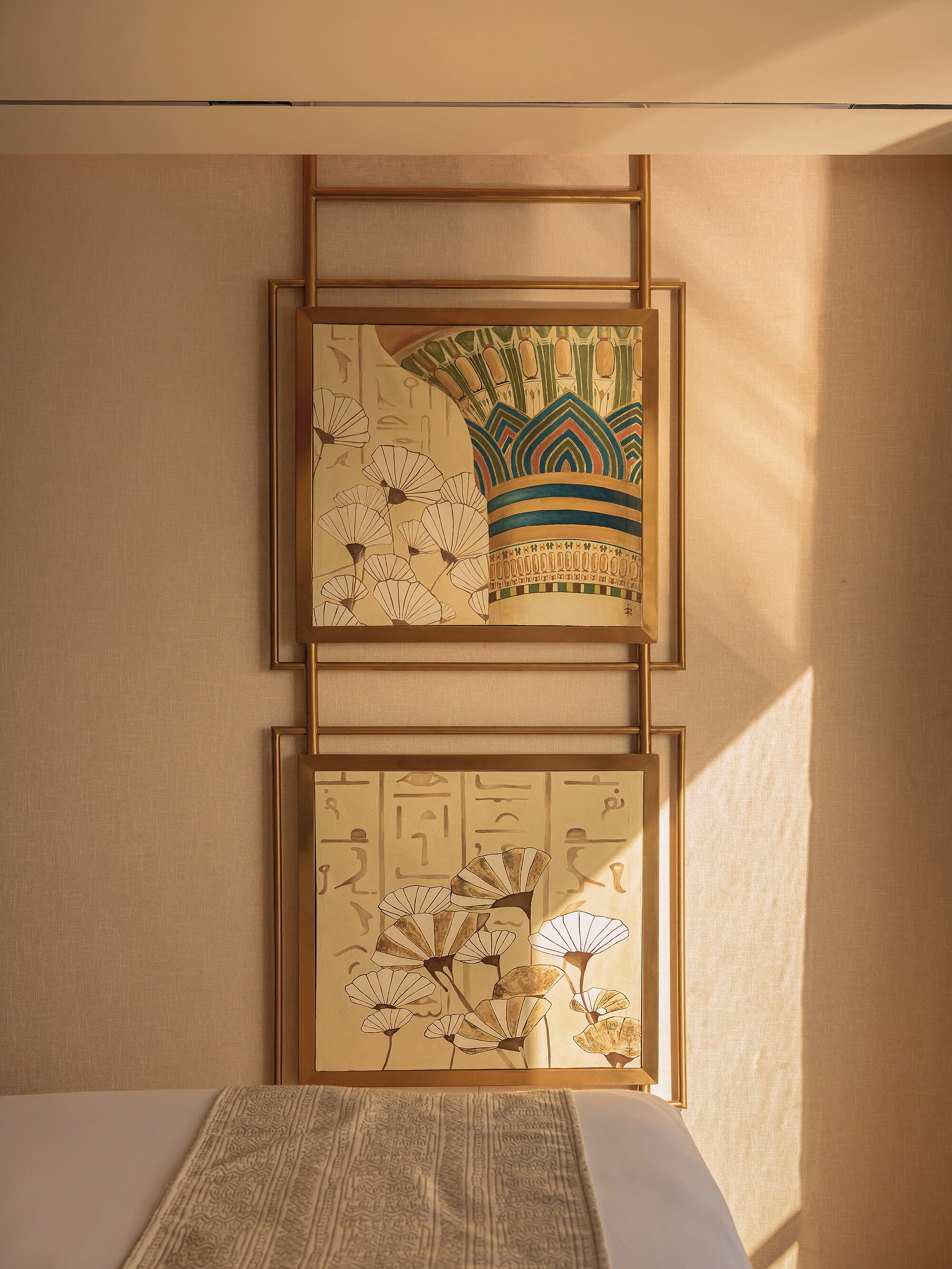 A room with a bed, a wall-mounted artwork depicting ancient Egyptian hieroglyphs, and a window casting a shadow.