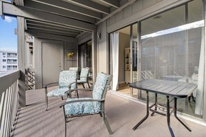 A balcony with two chairs and a table, a sliding glass door, and a view of the building's interior. - Ocean View Condominium 2 Bedroom Condo (Myrtle Beach)