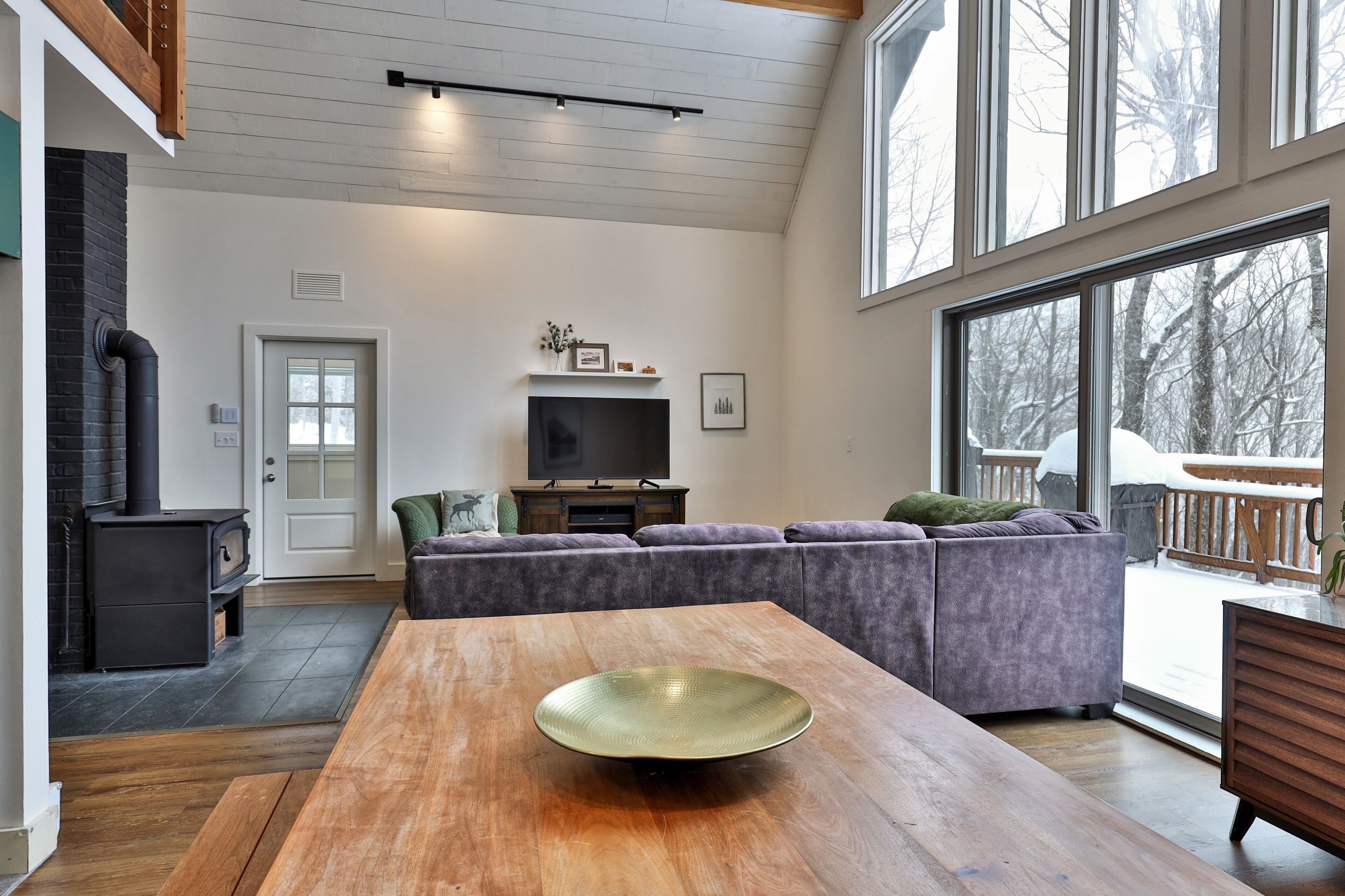 A modern living room with a large wooden dining table, a gray sectional sofa, and a TV on a wooden stand.