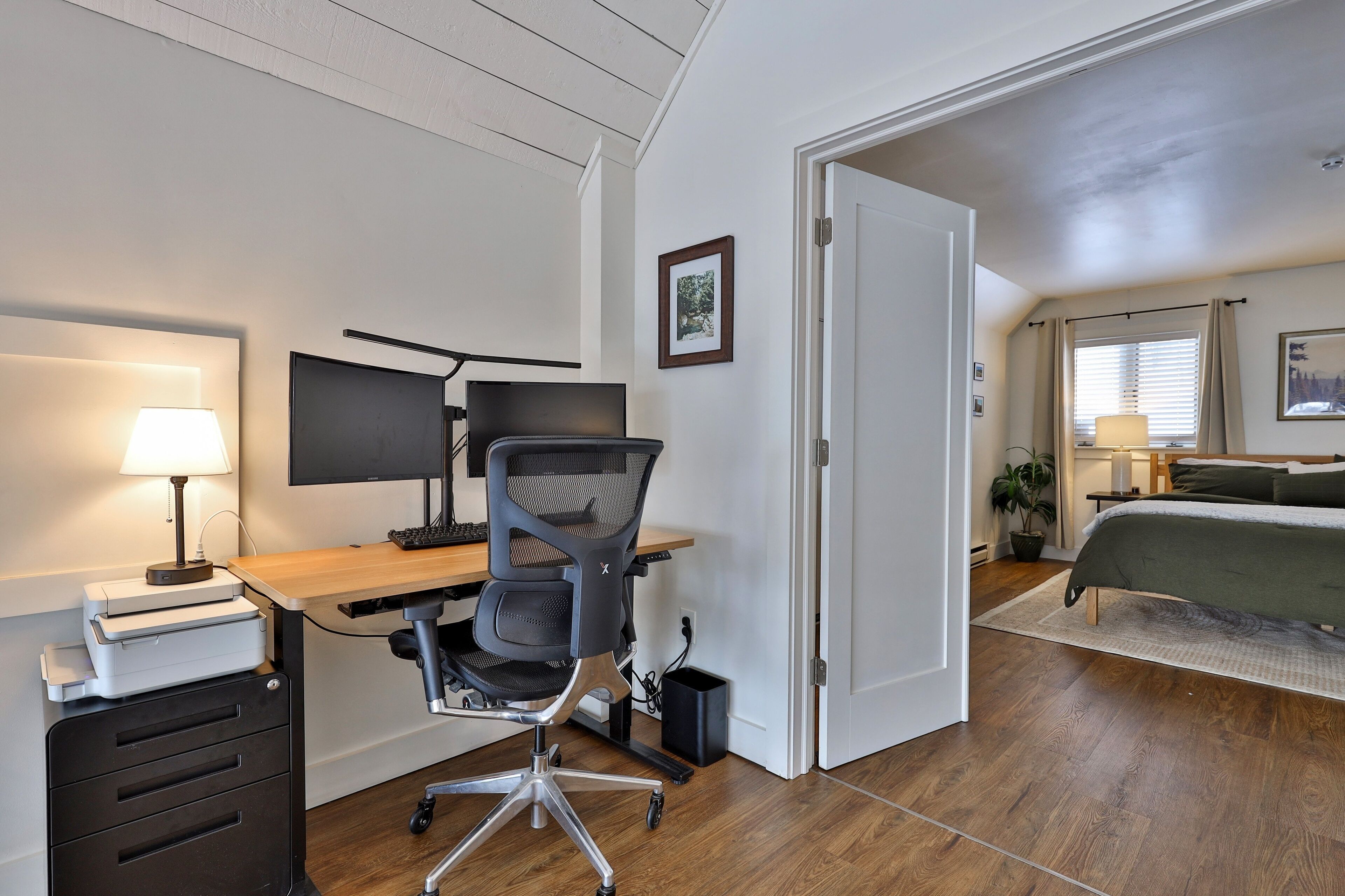 Een moderne slaapkamer met een houten bureau, een computer en een bed.