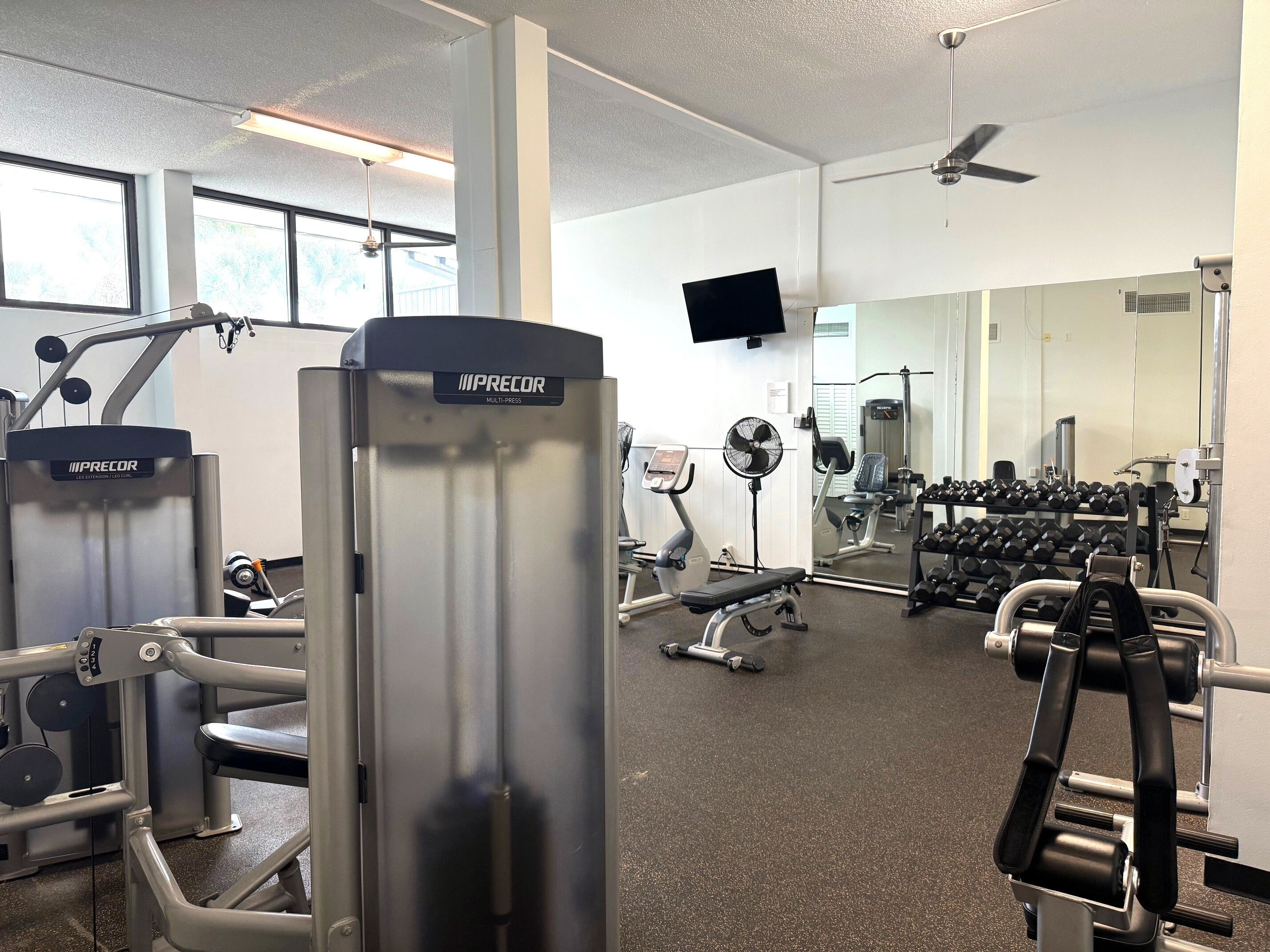 A gym with various exercise equipment, including a multi-press machine, treadmills, and dumbbells.