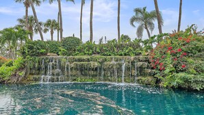 A waterfall cascading into a clear pool surrounded by lush greenery and tall palm trees. - Sole Retreat 2 Bedroom Condo (Siesta Key)