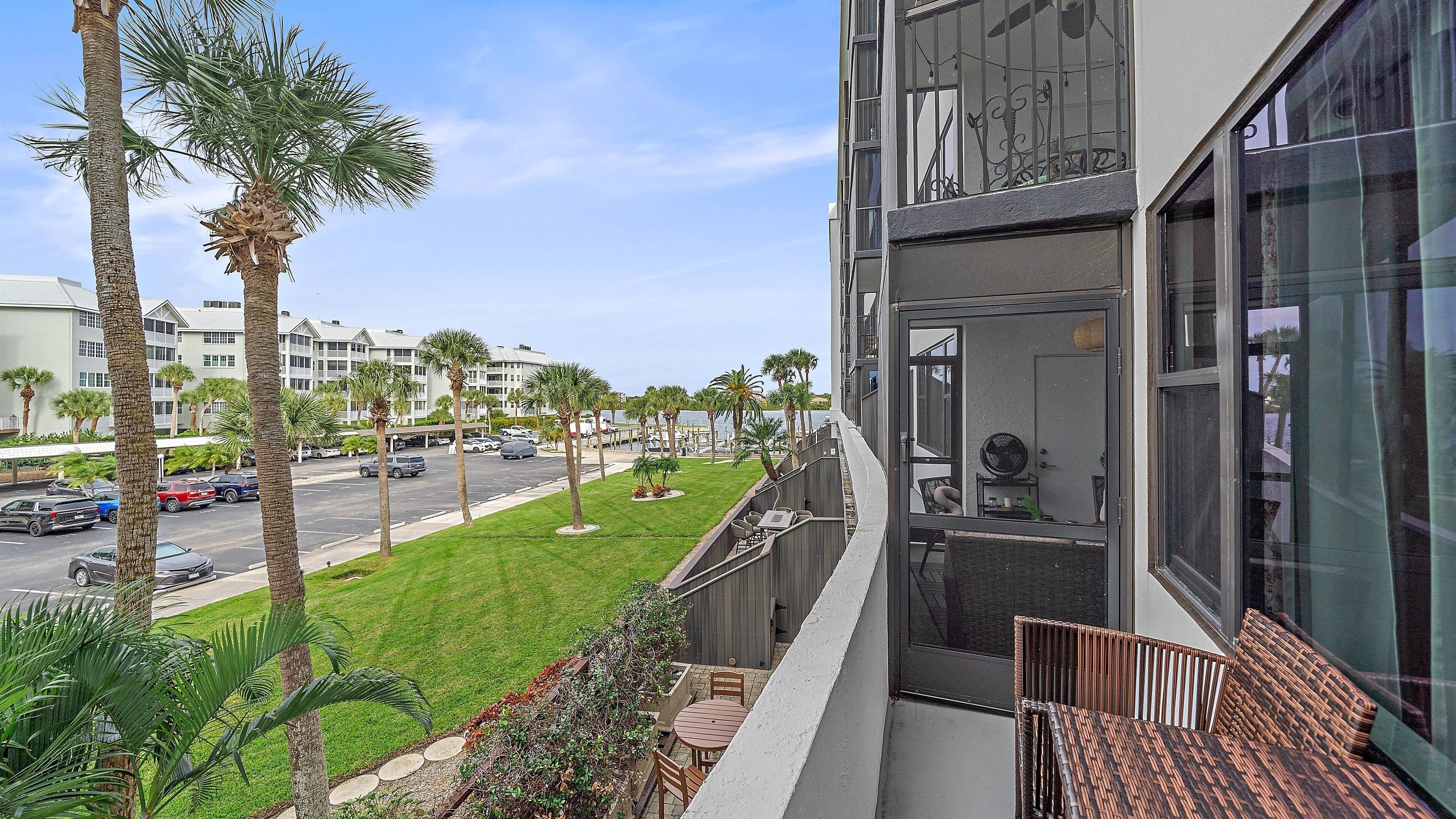 A balcony with a view of a parking lot, palm trees, and a marina.