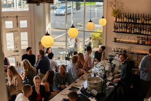A restaurant with a bar area, dining tables, and a view of the street through large windows. - The Italian Library: Amazing Views + Free Parking! (Carlton)