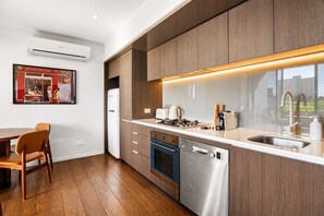 A modern kitchen with wooden cabinets, a built-in oven, a dishwasher, and a large window overlooking a cityscape. - The Italian Library: Amazing Views + Free Parking! (Carlton)