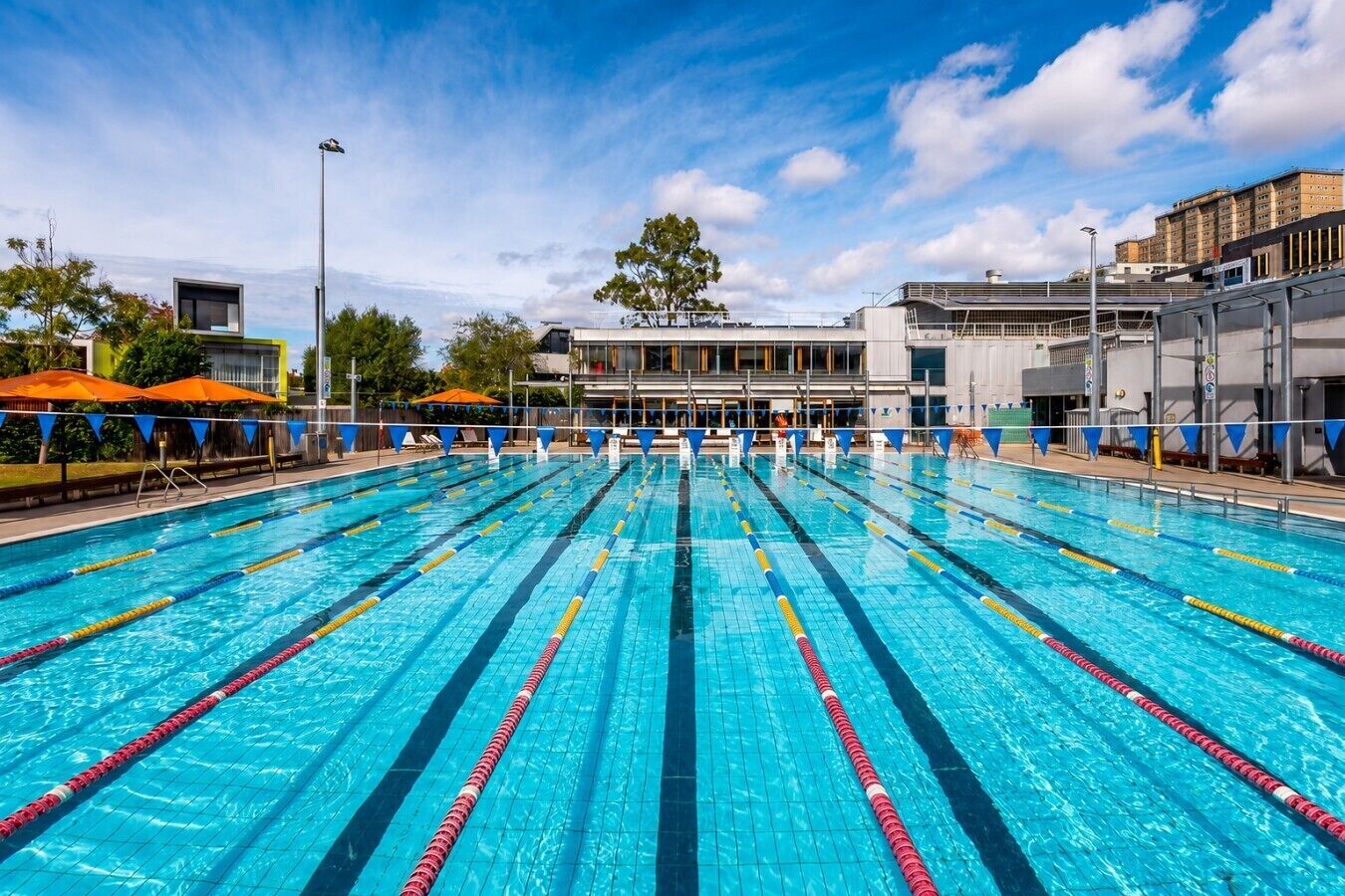 A swimming pool with multiple lanes, a building in the background, and a clear sky.