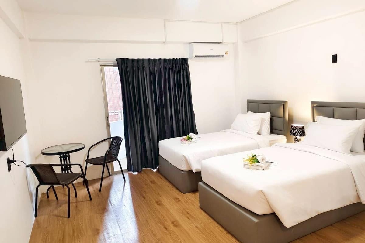 A hotel room with two beds, a small table, a chair, and an air conditioning unit.