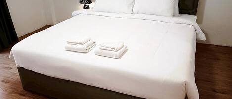 Un lit bien fait, avec des draps blancs et deux serviettes pliées posées sur le lit.