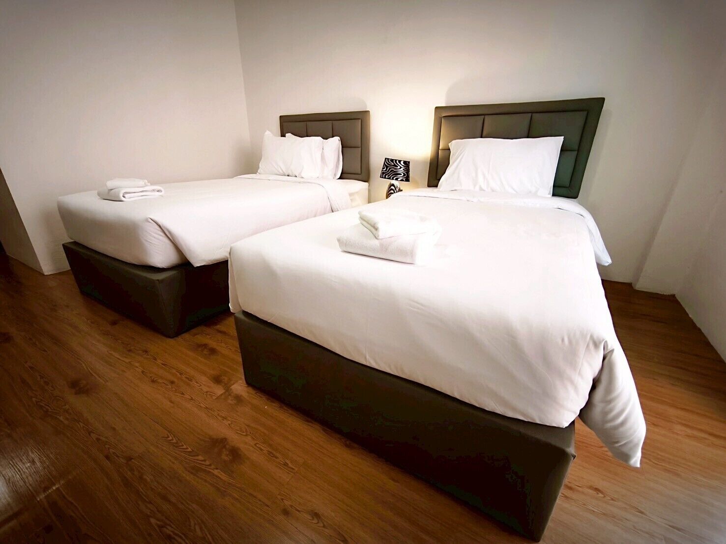Dos camas individuales con cabeceros, ropa de cama blanca y una mesita de noche con lámpara.