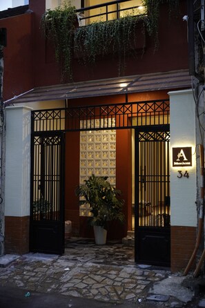 A gated entrance with a potted plant, a sign with the number 34, and a building with a red and white facade. - Little An Home (Ho Chi Minh City)