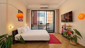 A modern bedroom with a bed, a red patterned rug, a potted plant, and a TV on the wall.