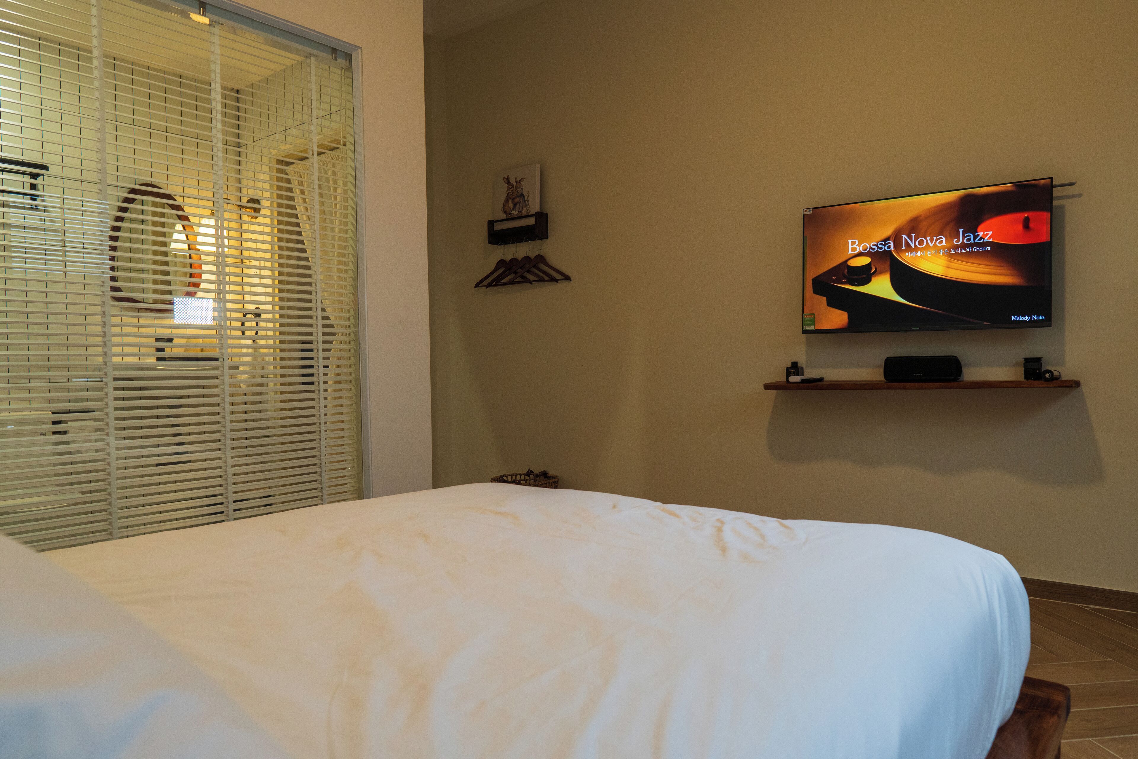 Een hotelkamer met een bed, een televisie op een standaard, een raam met zonwering en een aan de muur hangend schilderij.