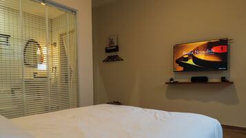 Een hotelkamer met een bed, een televisie op een standaard, een raam met zonwering en een aan de muur hangend schilderij.