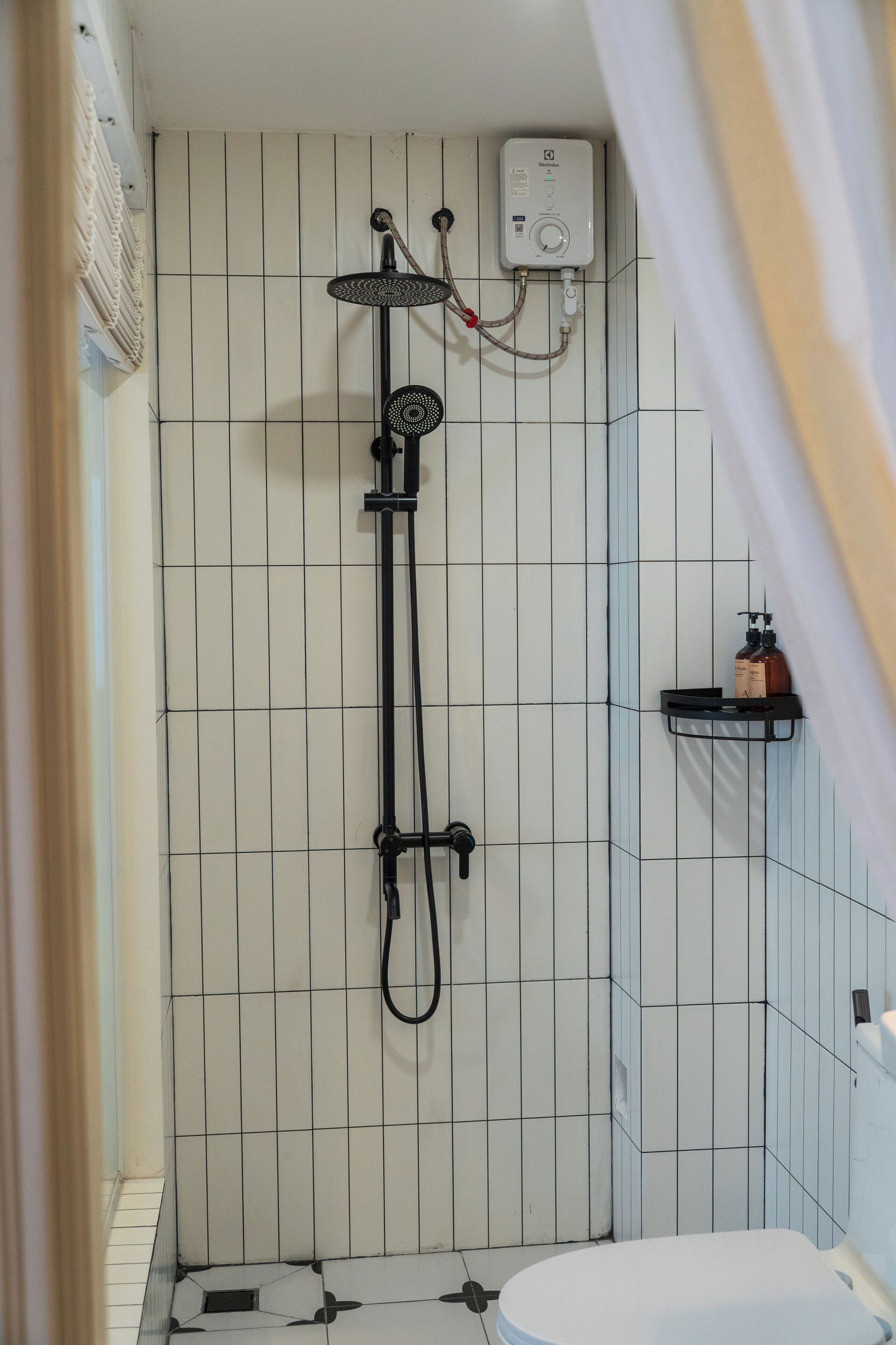 A bathroom with a shower, toilet, and a small shelf with toiletries.