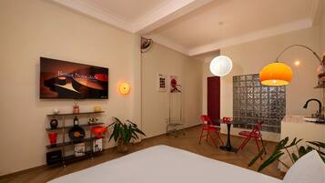 A modern hotel room with a large bed, a TV displaying 'Bossa Nova Jazz', a red chair, a small table, and a decorative wall with a patterned window.