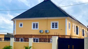 A two-story house with a dark roof, white-framed windows, and a gated entrance.