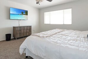 A bedroom with a bed, a television mounted on the wall, a window with blinds, and a wooden dresser. - Pet-Friendly 4BR Casa Grande Home | Private Pool (Casa Grande)