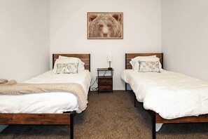 Ein Schlafzimmer mit zwei Einzelbetten, einem Nachttisch, einer Lampe und einem Bären-Motiv an der Wand.