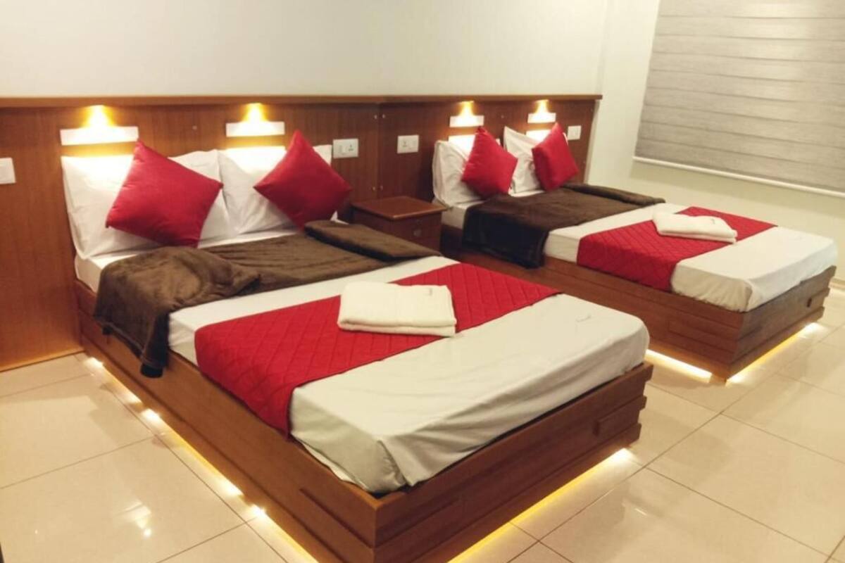 A hotel room with four beds arranged in a row, each with a wooden headboard and red and white bedding.