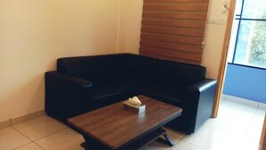 A black leather sofa, a wooden coffee table, and a window with blinds. - Emerald Royal Residency (Aluva)