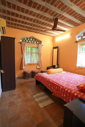 A bedroom with a brick ceiling, a bed with a polka dot bedspread, a window with curtains, a mirror, and a small stool. - Urban Tripper Aamar Bari Homestay by Arindam (Bolpur)