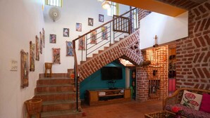 Un salón espacioso con una escalera que sube a un nivel superior, un televisor, muebles de mimbre y varias obras de arte en las paredes.