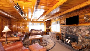 A log cabin interior with a fireplace, leather furniture, and a stone wall. - A Cabin on High - In Town - Fireplace - Mountain Views (Red River)