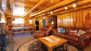 A log cabin interior with a wooden dining table, leather sofas, a coffee table, and a patterned rug. - A Cabin on High - In Town - Fireplace - Mountain Views (Red River)