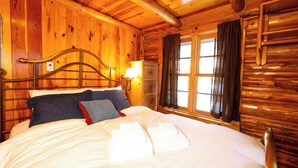 A wooden cabin interior with a bed, curtains, and a lamp. - A Cabin on High - In Town - Fireplace - Mountain Views (Red River)