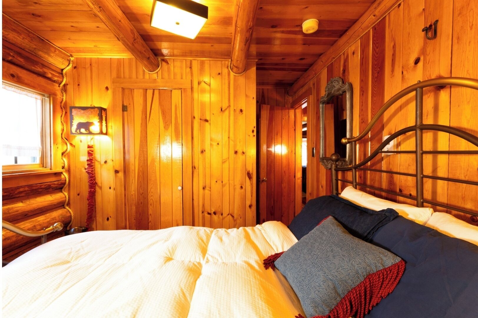 A wooden cabin interior with a bed, a mirror, and a window.