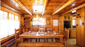 A wooden cabin interior with a dining table set for six, a chandelier, and a kitchen area. - A Cabin on High - In Town - Fireplace - Mountain Views (Red River)