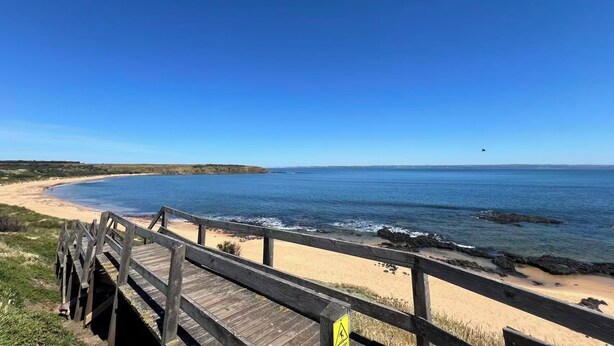 Una passerella in legno che conduce a una spiaggia sabbiosa con vista sull'oceano.