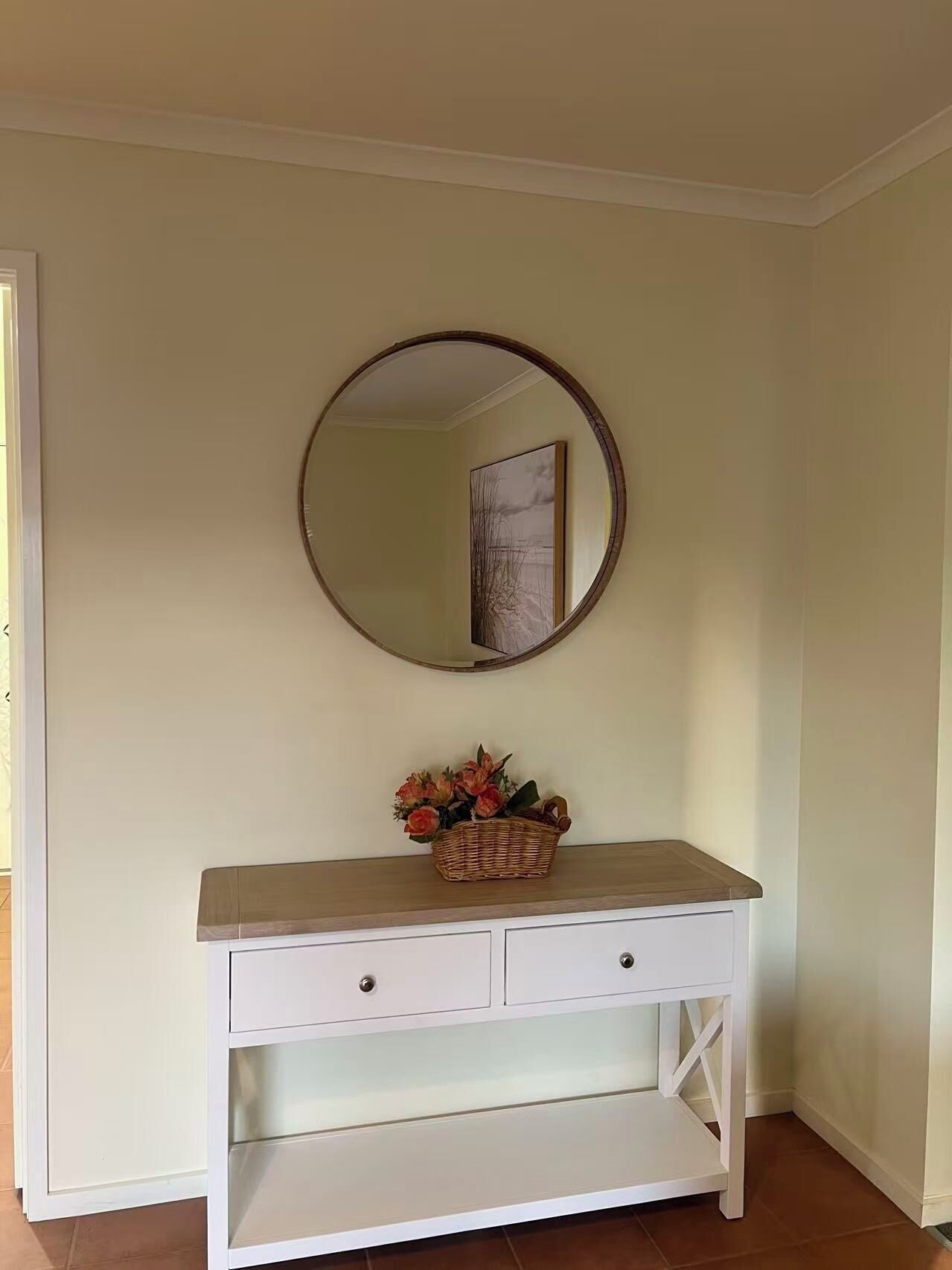 A white vanity with a mirror above it and a basket of flowers on the counter.
