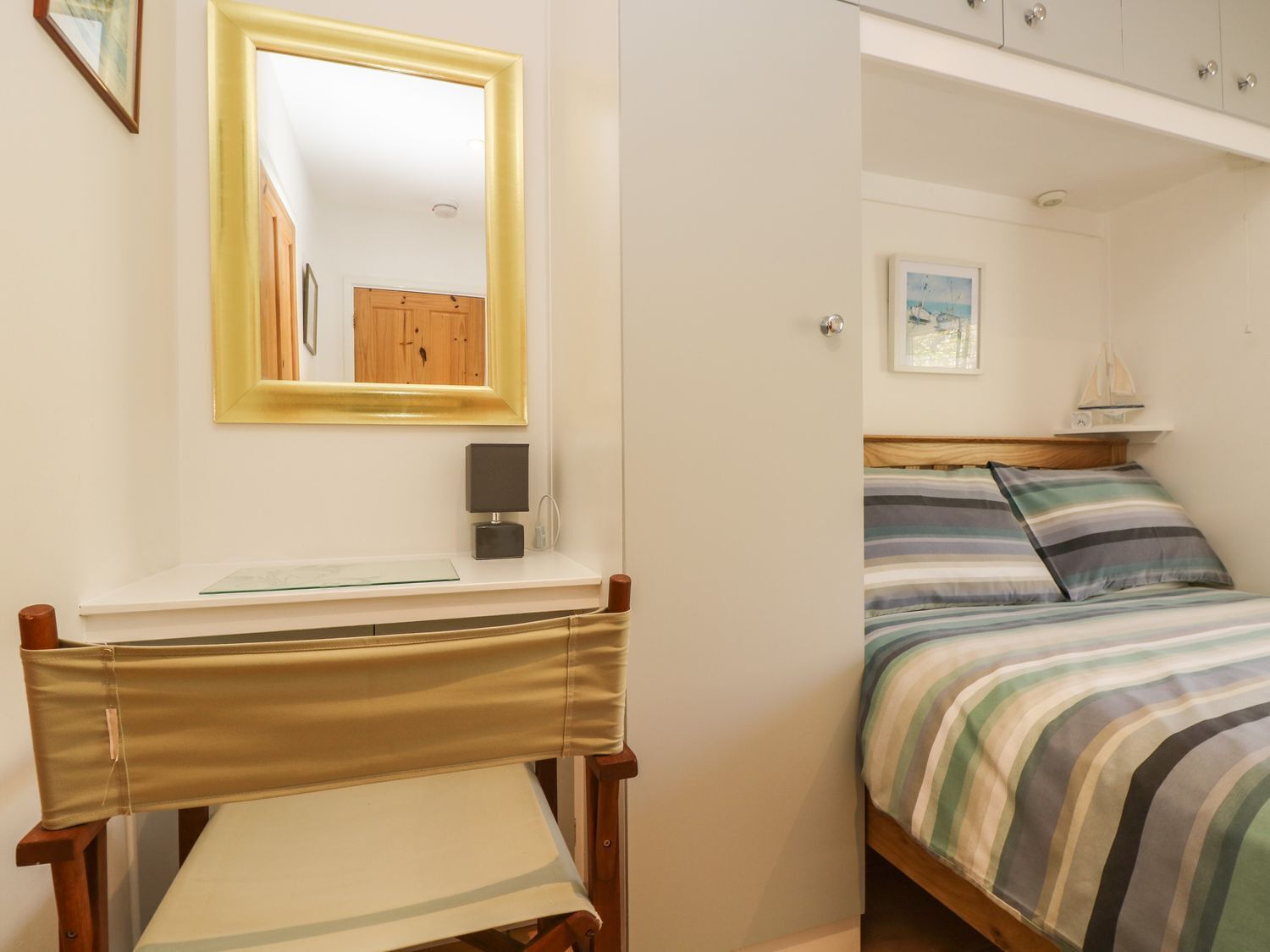 A bedroom with a bed, a bedside table, a mirror, and a window with a view of the sea.