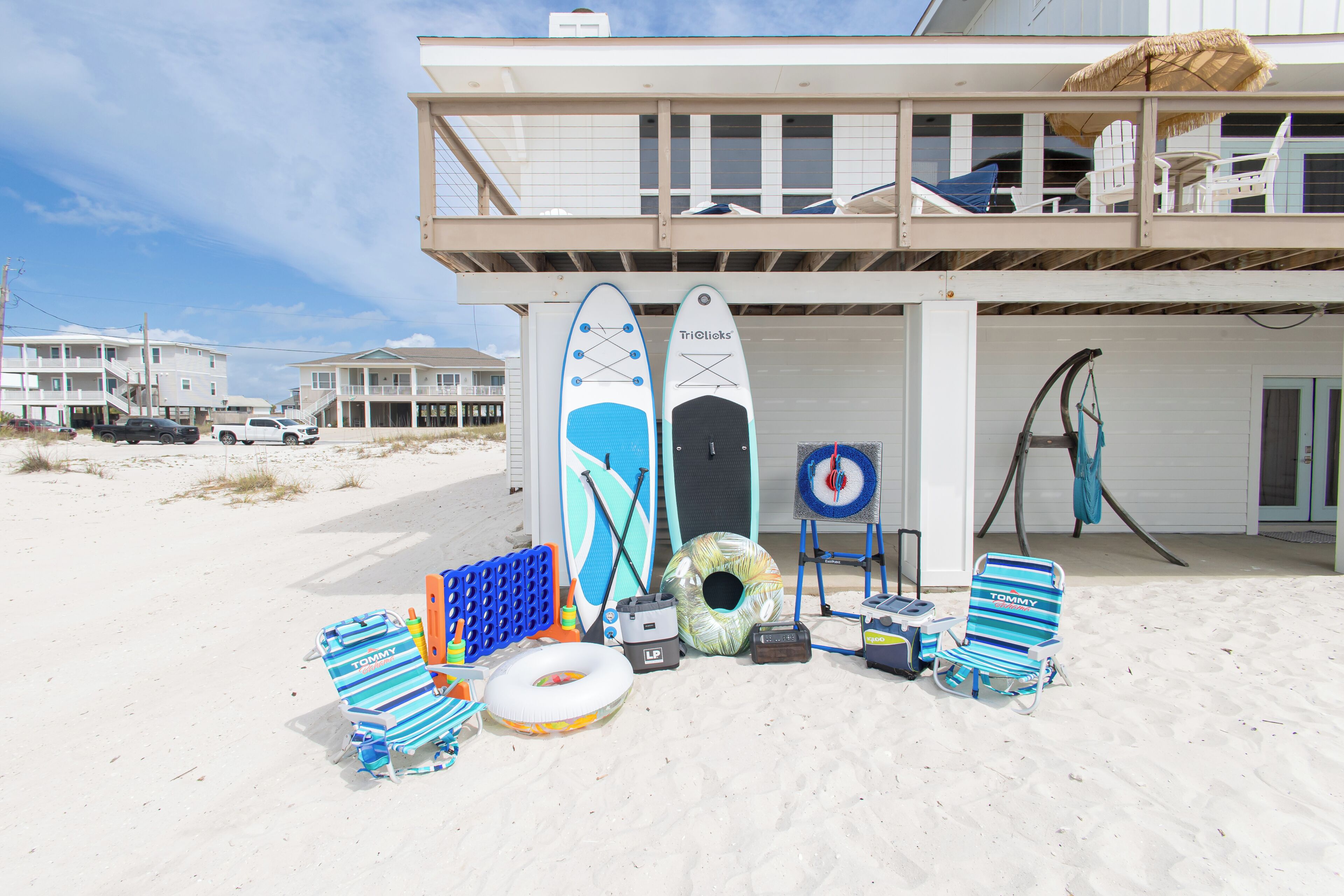 A beach house with a balcony, a pool, and various beach items like a surfboard, lounge chair, and inflatable ring.
