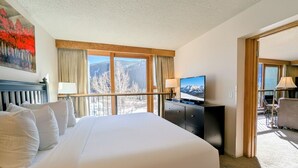 A hotel room with a large bed, a television, a desk, and a view of mountains through the window. - Keystone Lake Escape | Trails + Paddle + Relax (Keystone)