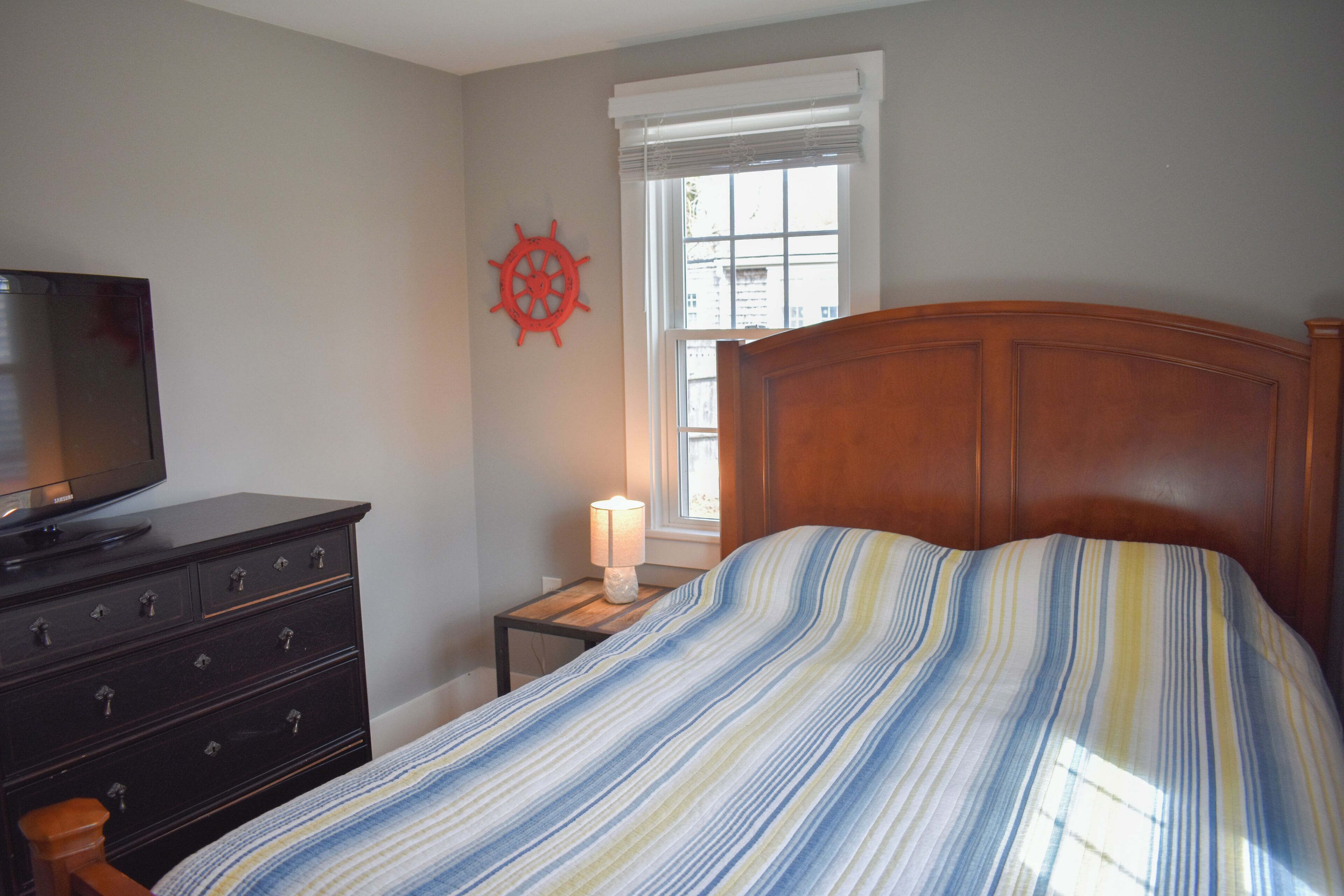 Un dormitorio con cama, cómoda, televisor, ventana y un adorno en la pared.